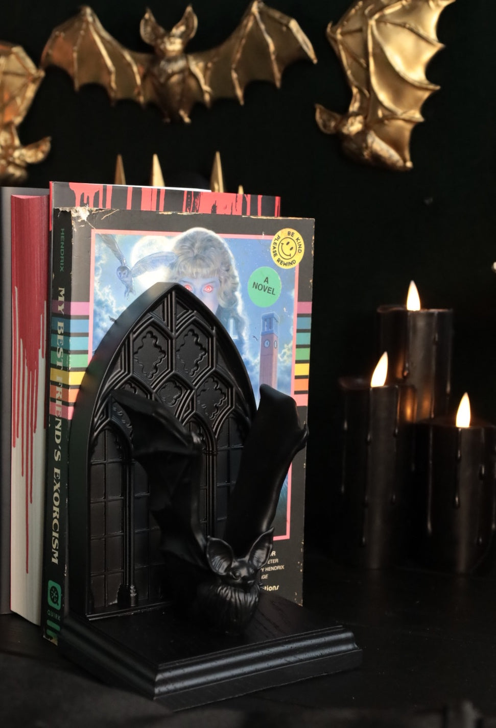 Black bat bookend on a stack of books with candles and decorative bats in the background