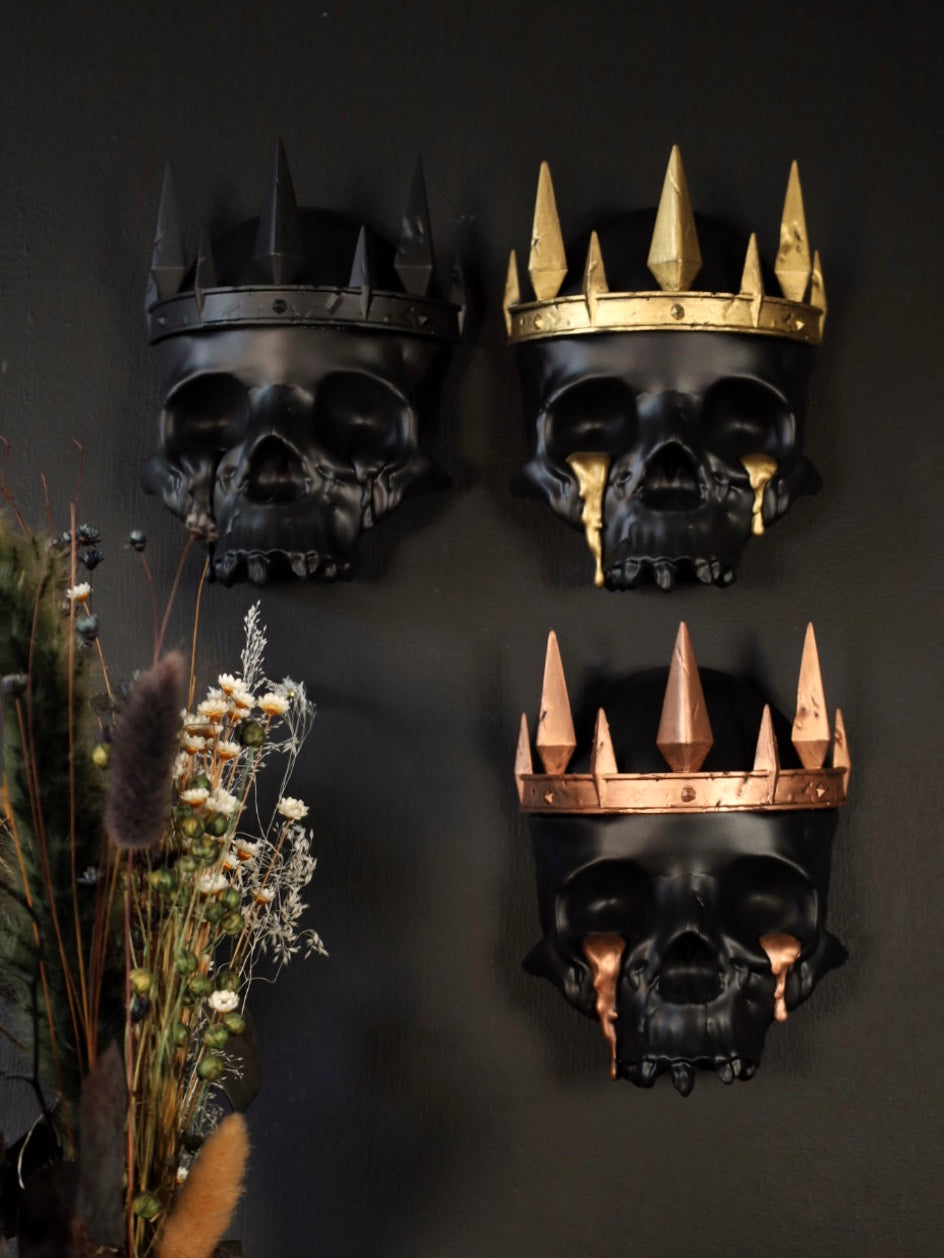 Three decorative gothic skull wall hangings with crowns on a gothic gallery wall