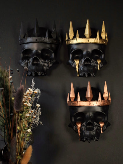 Three decorative gothic skull wall hangings with crowns on a gothic gallery wall