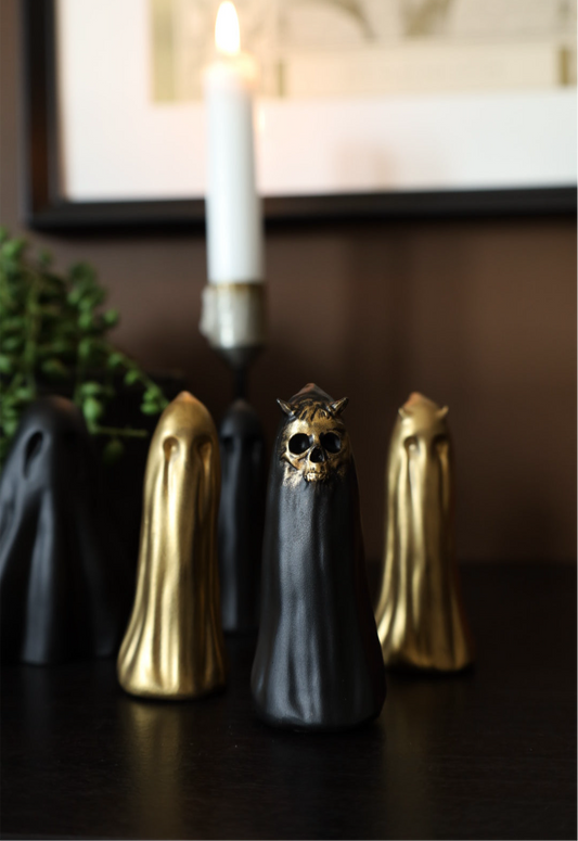 Decorative gothic skull ornament with gold and black finishes on a dark surface, with a candle in the background.