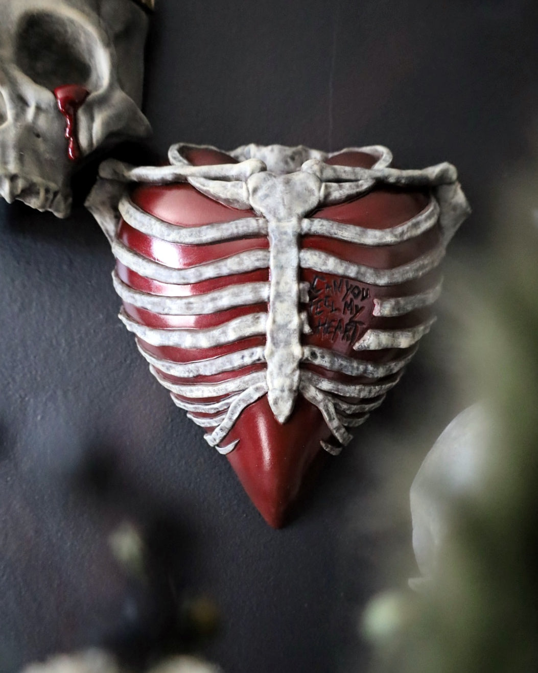 A gothic style wall plaque shaped like a ribbed human chest with a glossy red heart and weathered bones