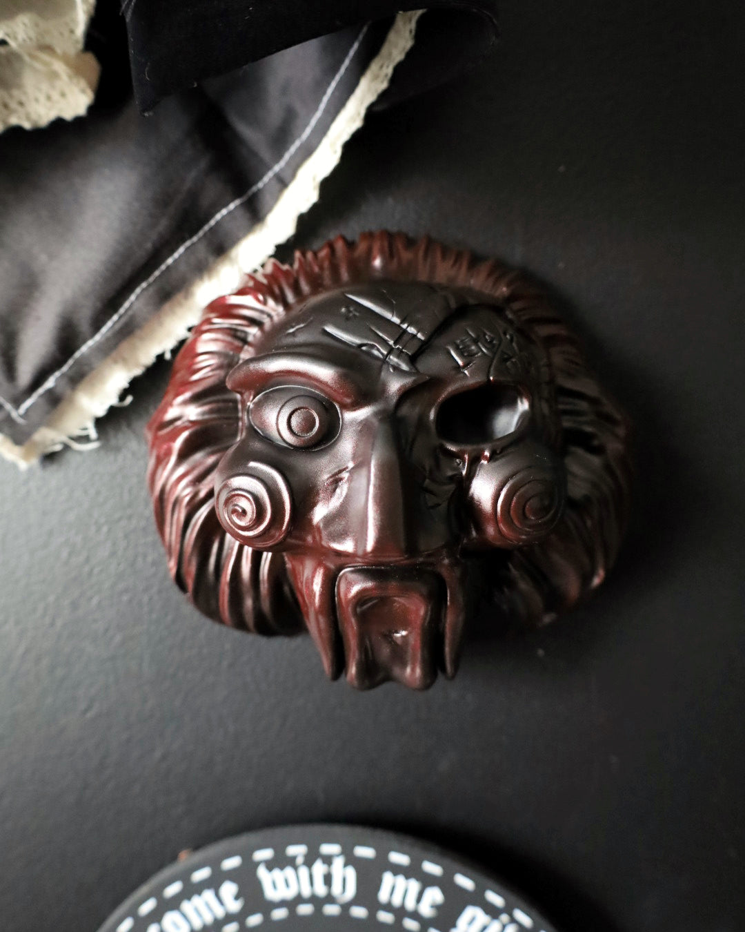 A dark red/black fade jigsaw character with spiral eyes and a wide open mouth, from the Saw movies