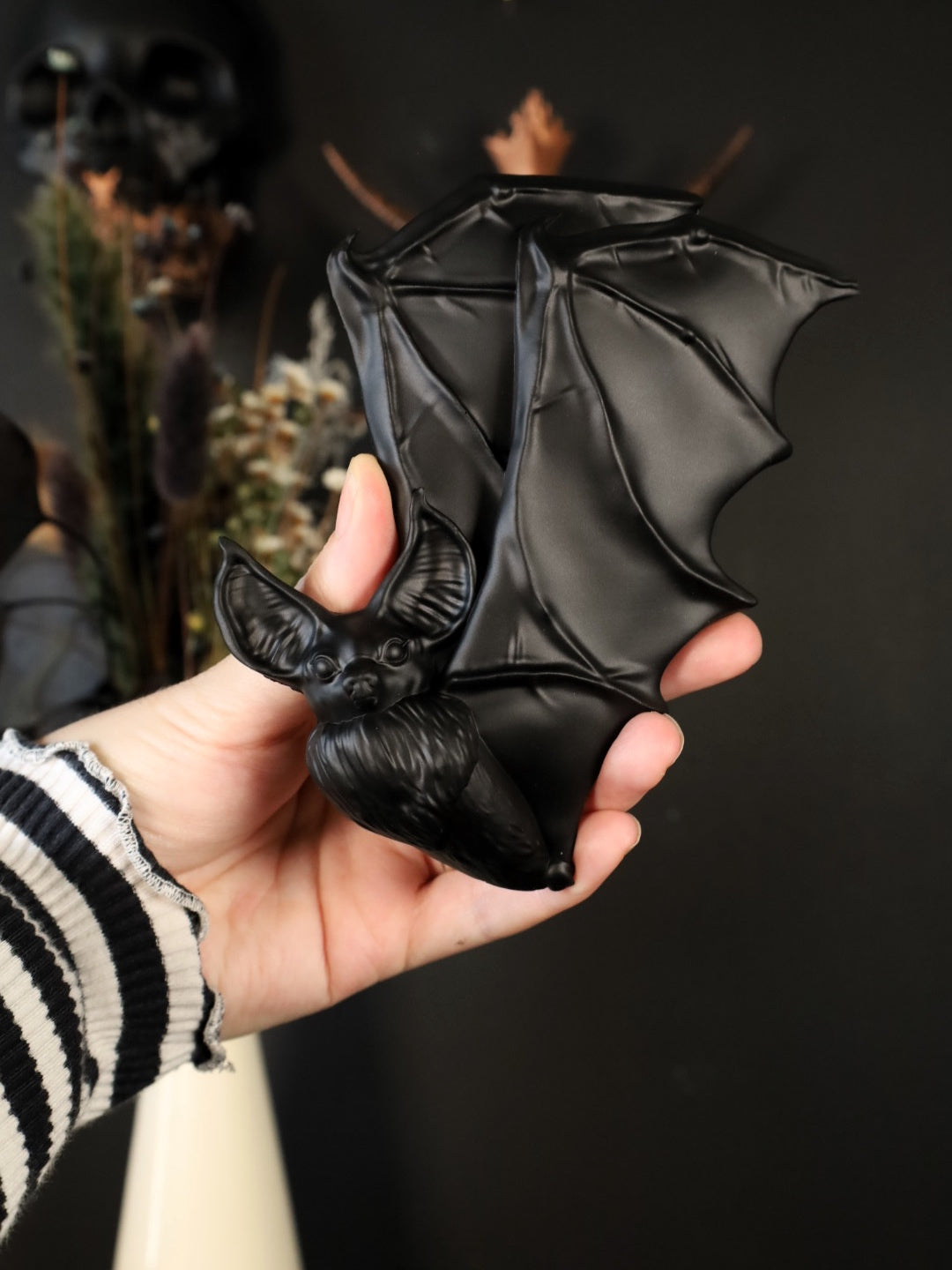 Hand holding a black flying bat wall hanging against a dark background