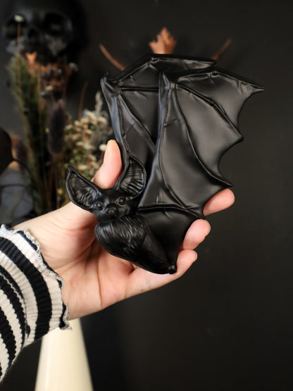 Hand holding a black flying bat wall hanging against a dark background