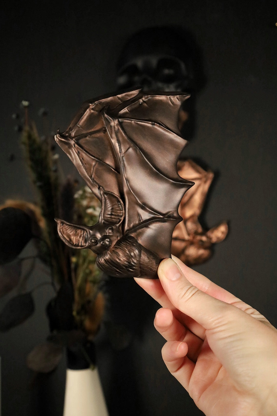 Antique brown left facing flying bat held by a hand against a dark background