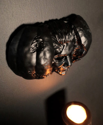 Hand holding a Halloween pumpkin with a Michael Myers face mask inside against a dark background