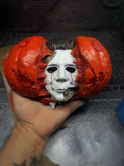 Hand holding a Halloween pumpkin with a Michael Myers face mask inside against a dark background