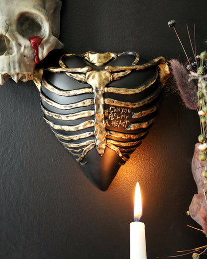 A gothic style wall sconce for your gothic gallery wall shaped like a ribcage over a heart, featuring a black and gold metallic finish.