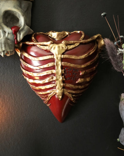 A gothic style wall sconce for your gothic gallery wall shaped like a ribcage over a heart, featuring a red and gold metallic finish.