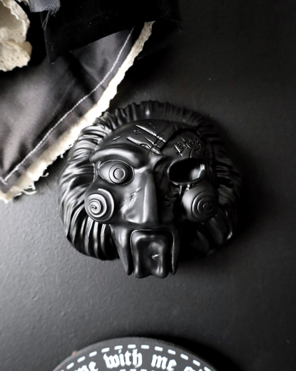 A black painted jigsaw character with spiral eyes and a wide open mouth, from the Saw movies
