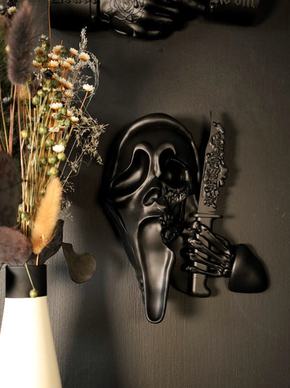 Scream Ghostface mask with a knife and hand holding it against a dark background