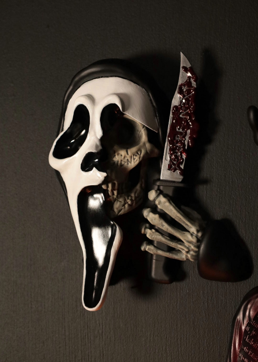 Scream Ghostface mask with a knife and hand holding it against a dark background