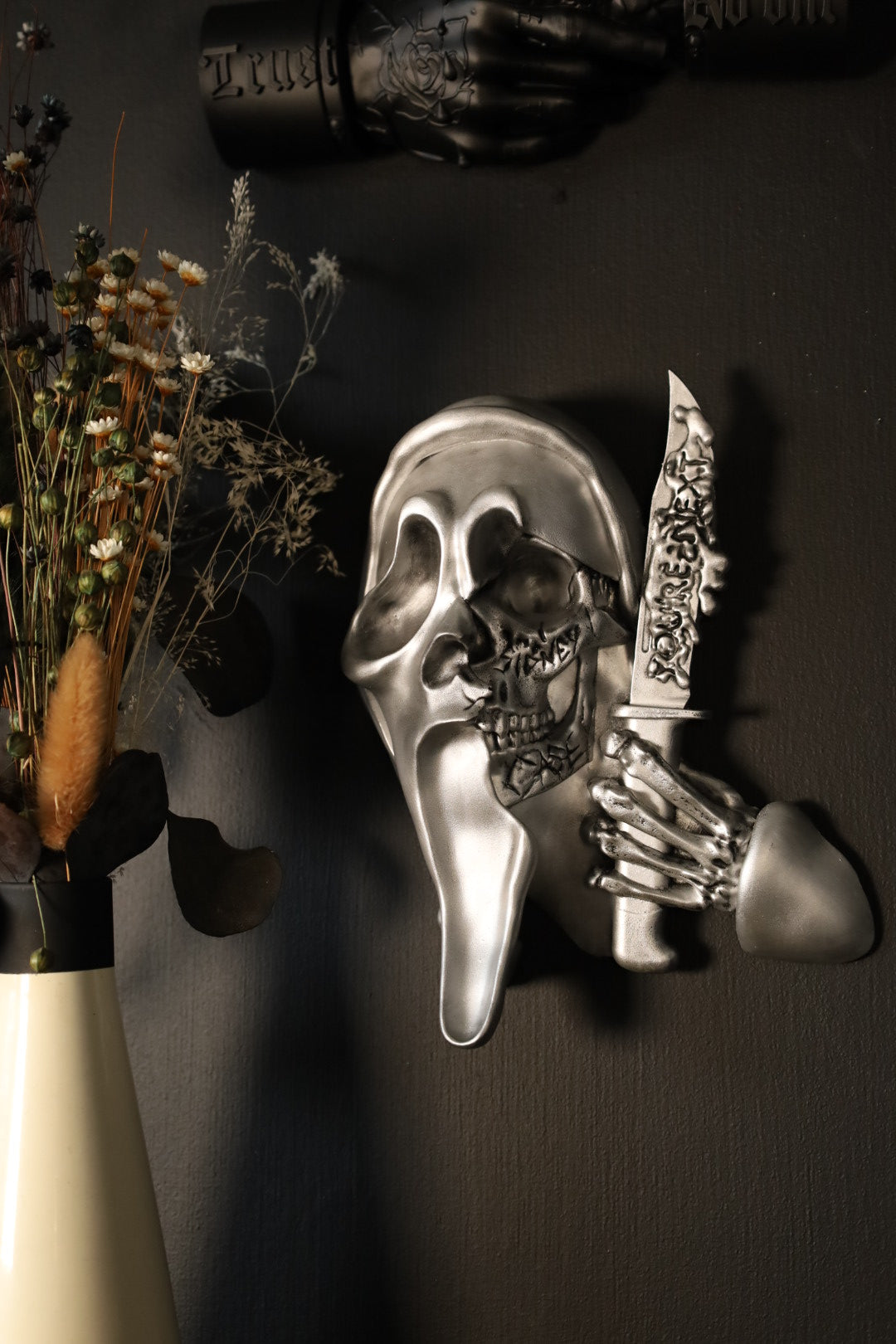 Scream Ghostface mask with a knife and hand holding it against a dark background