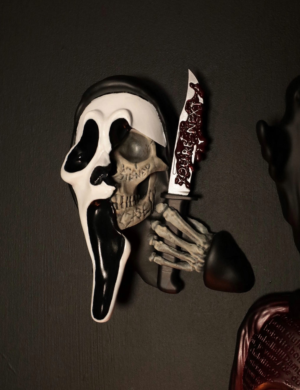 Scream Ghostface mask with a knife and hand holding it against a dark background