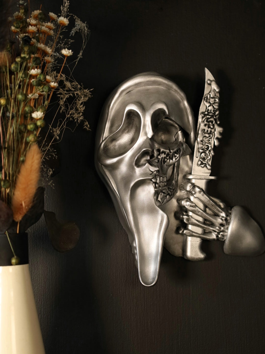Scream Ghostface mask with a knife and hand holding it against a dark background