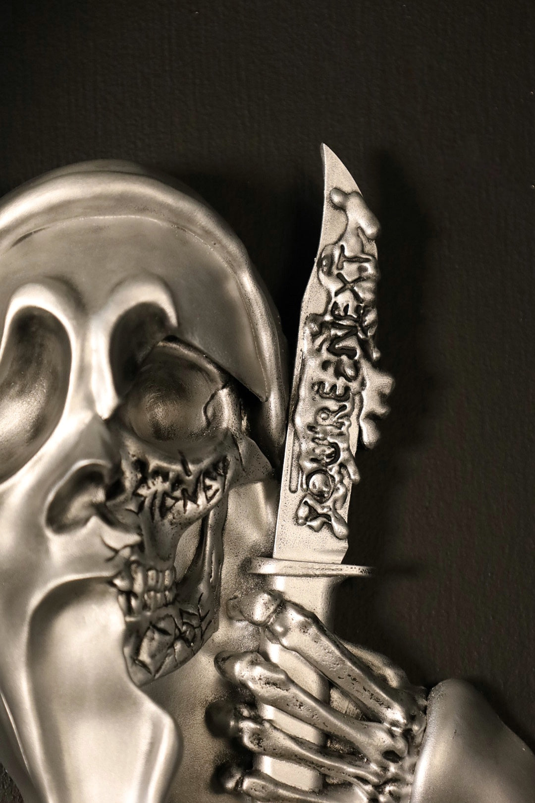 Scream Ghostface mask with a knife and hand holding it against a dark background