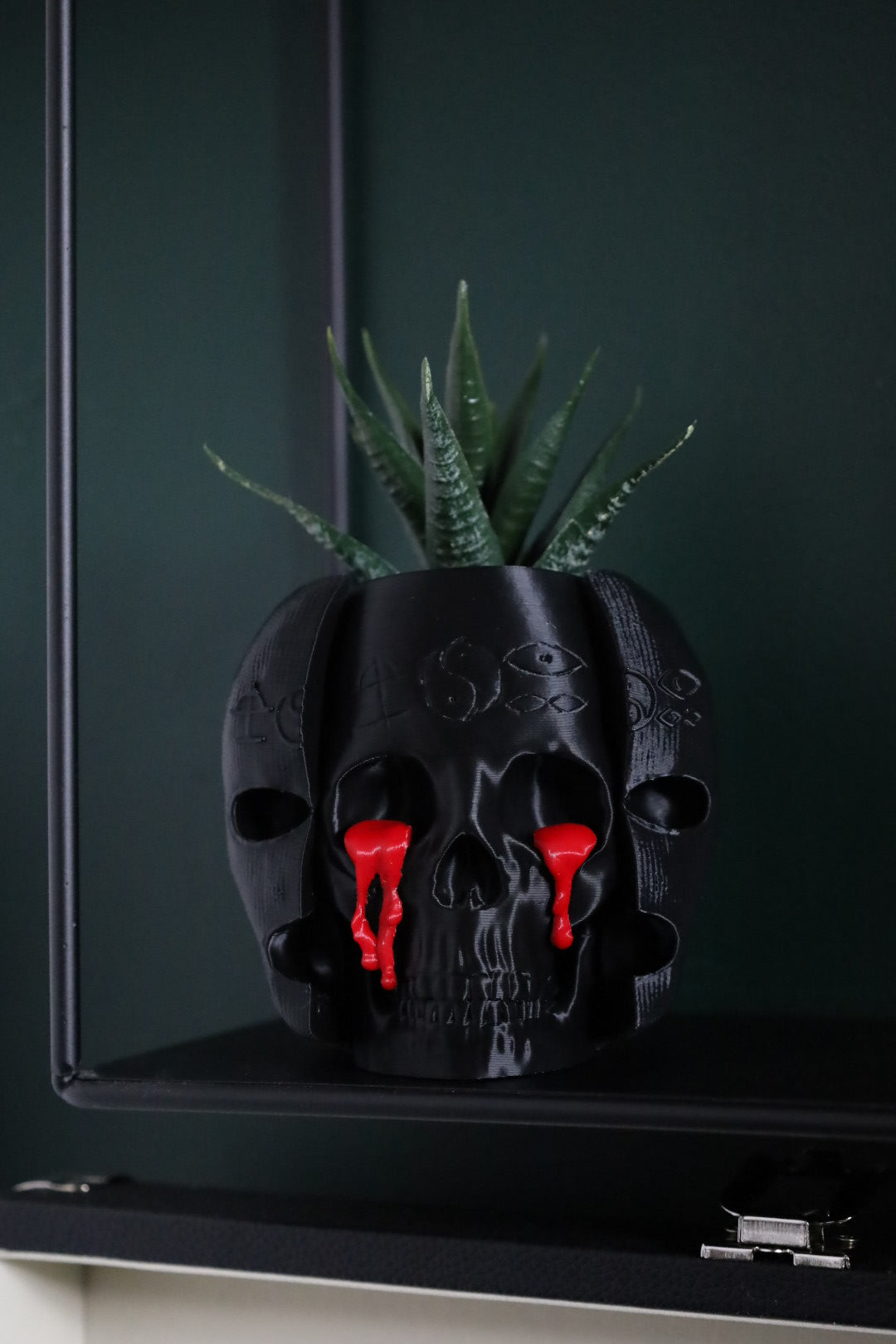A gothic black skull planter with a plant growing out of it. Inspired by the band Bad Omens 