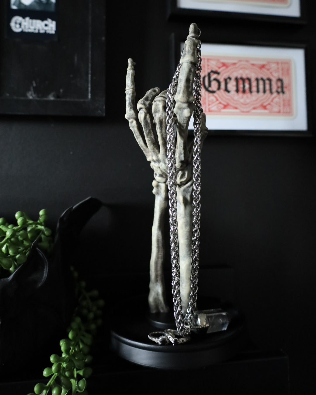 A skeleton hand jewellery stand or ornament holding silver chains and rings, set on a black round base.