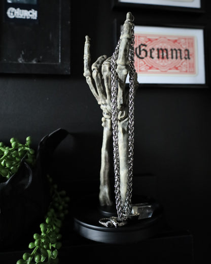 A skeleton hand jewellery stand or ornament holding silver chains and rings, set on a black round base.