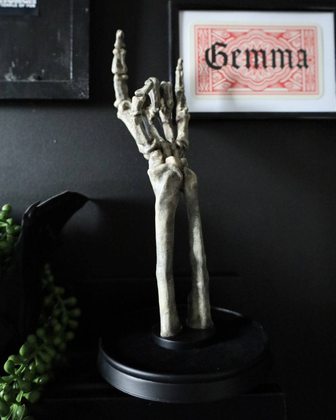 A skeleton hand jewellery stand or ornament holding silver chains and rings, set on a black round base.