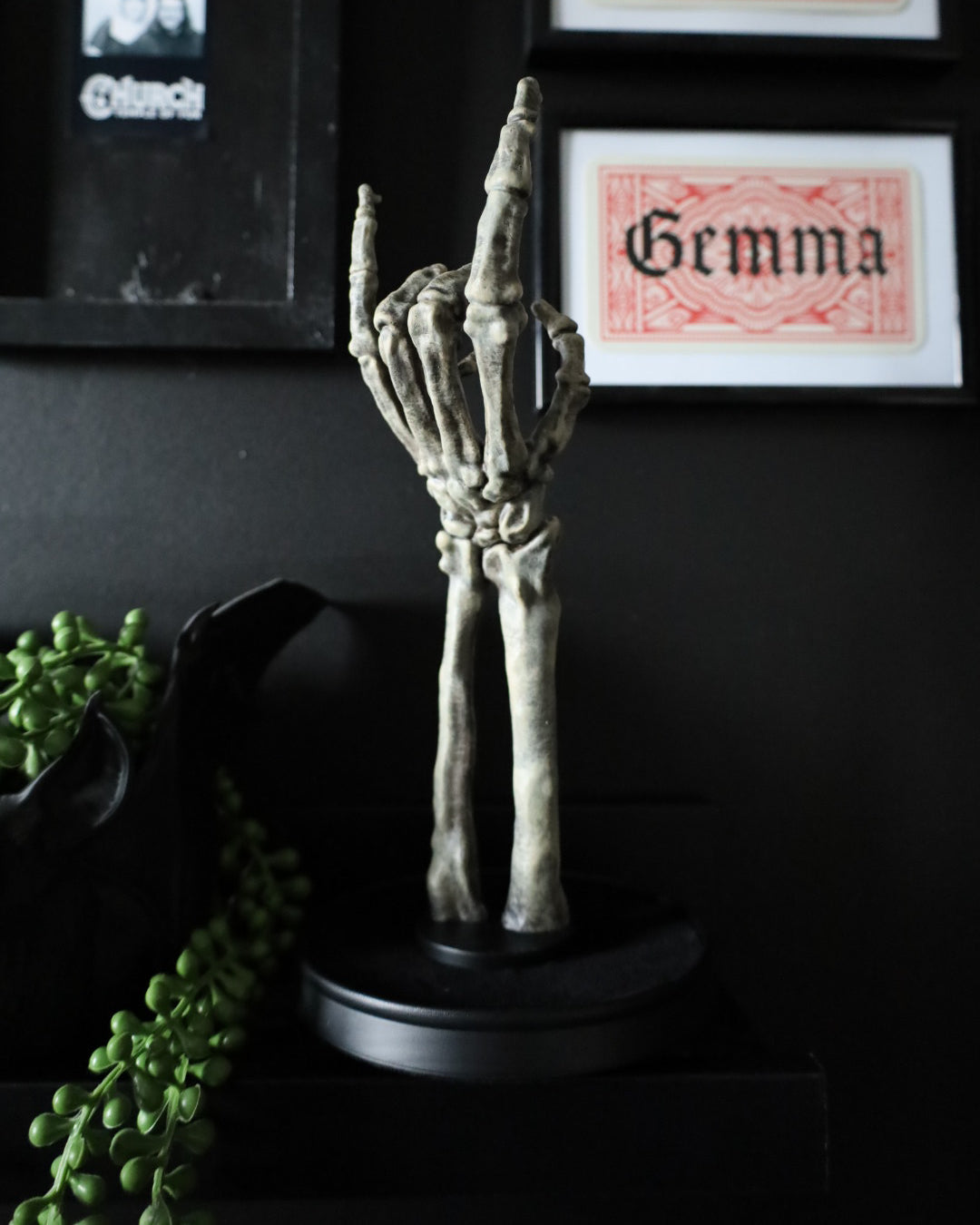 A skeleton hand jewellery stand or ornament holding silver chains and rings, set on a black round base.