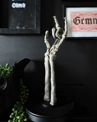 A gothic skeleton hand jewellery stand or ornament holding silver chains and rings, set on a black round base.