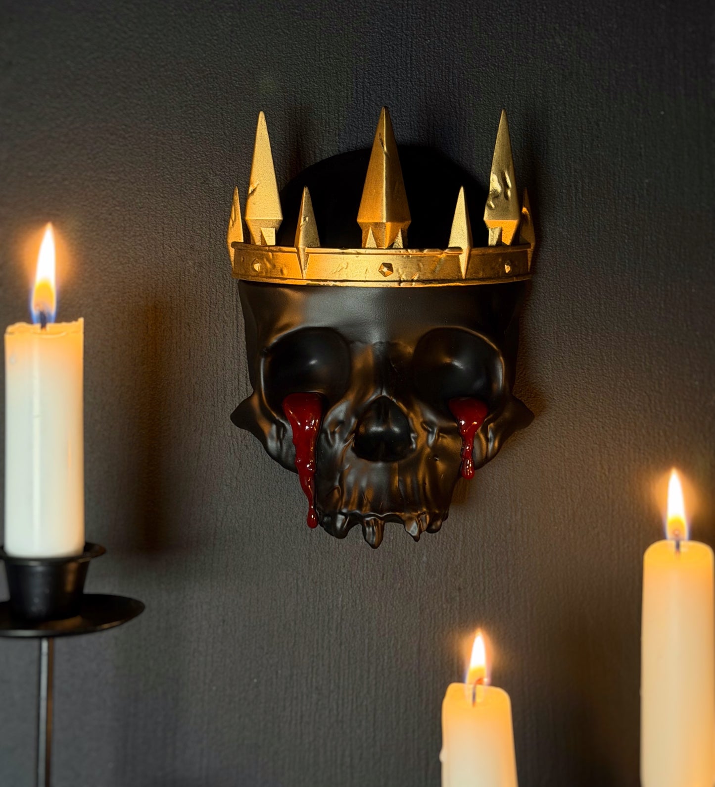 Decorative skull wall art with a gold crown and blood like tears on a gothic gallery wall