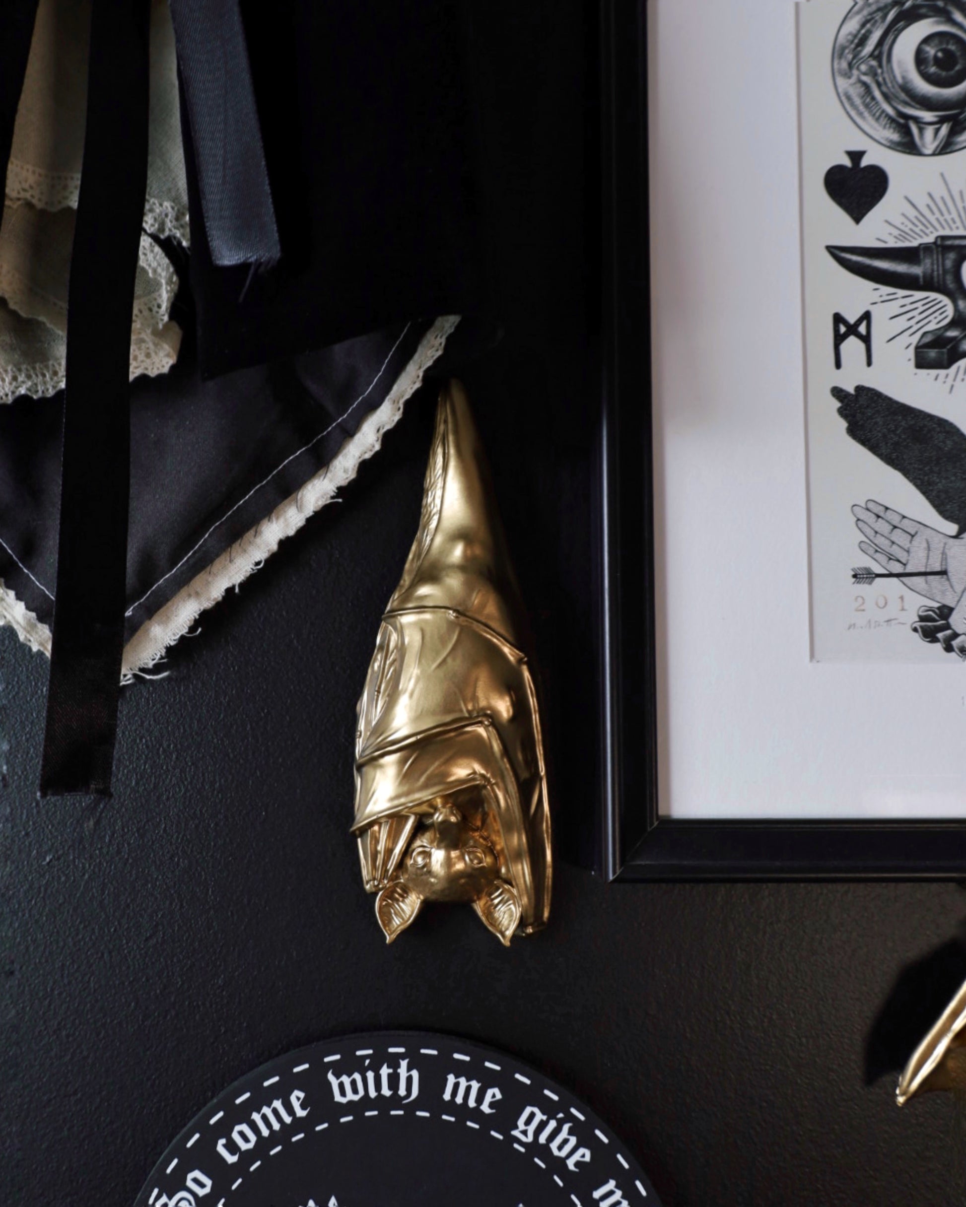 Gold sleeping hanging bat decorative wall hanging on a black wall with framed artwork