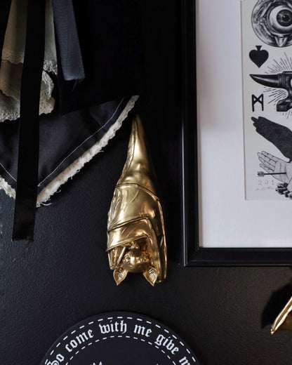 Gold sleeping hanging bat decorative wall hanging on a black wall with framed artwork