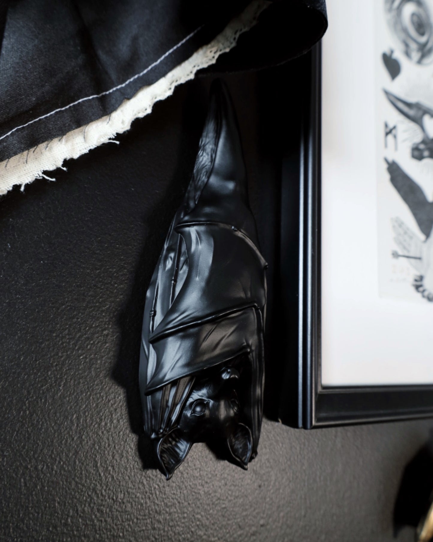 Black hanging sleeping bat decoration on a dark wall next to a framed picture