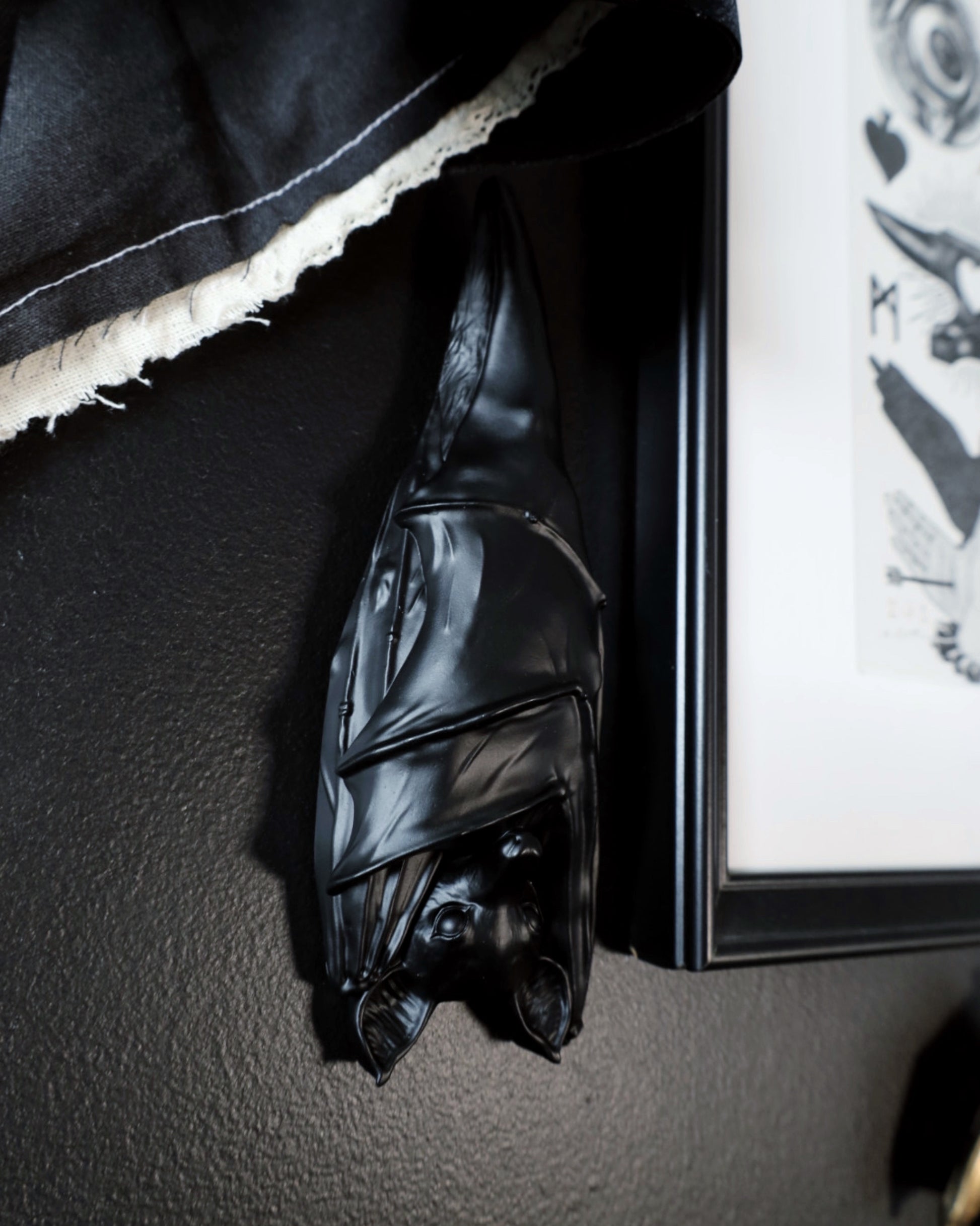 Black hanging sleeping bat decoration on a dark wall next to a framed picture