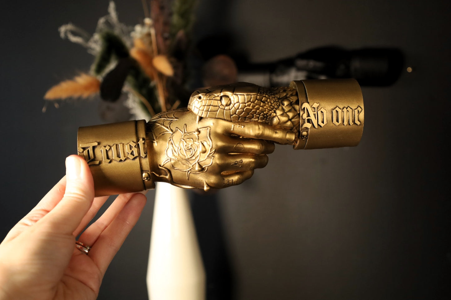 A tattooed hand wall hanging with a snake biting and the text trust no one. 