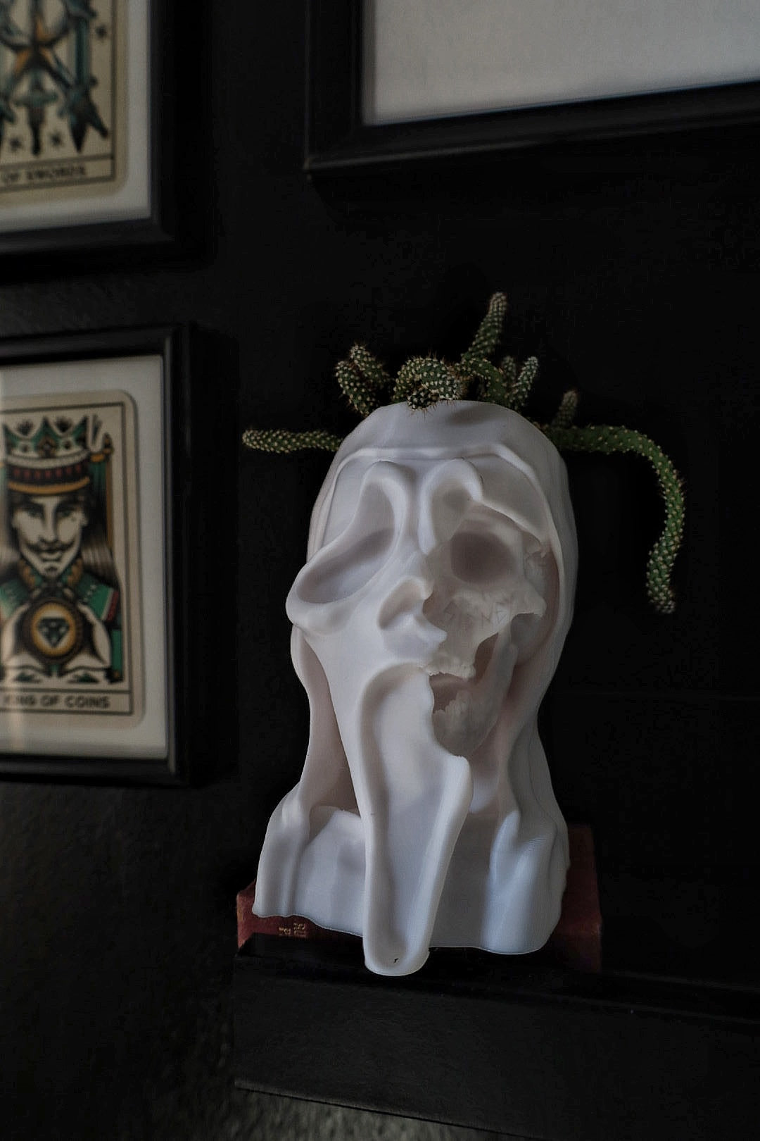 White ceramic head sculpture on a dark surface with framed artwork in the background