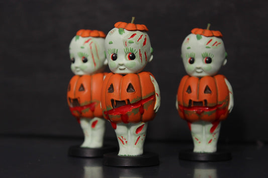 A set of three hand painted Halloween ornaments from the Kreepy Collection, featuring zombie themed pumpkin designs with orange clothing and green decaying skin.